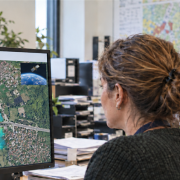 Two infrastructure managers examine an illustrative ground deformation map on a monitor, with a small satellite image in the corner.
